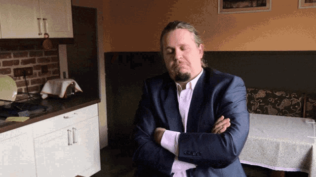 a man in a suit is sitting with his arms crossed in a kitchen