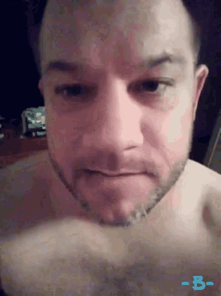 a shirtless man with a beard looks at the camera with the letters b- on the bottom