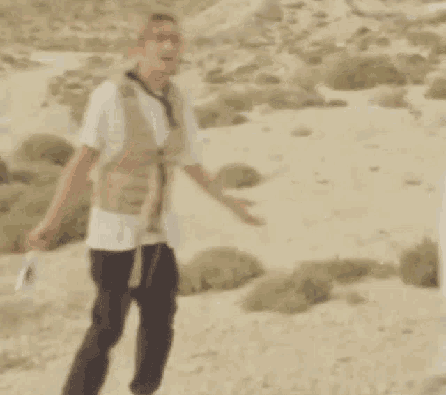 a man in a vest is standing in a desert holding a camera .
