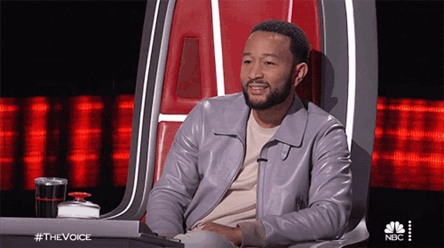 a man in a purple leather jacket is sitting in a chair with a nbc logo behind him