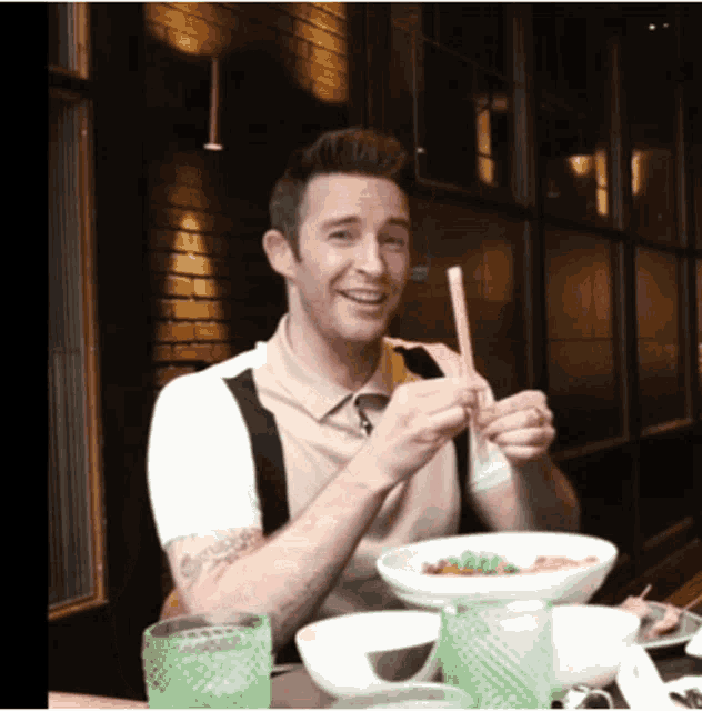 a man is sitting at a table with a bowl of food and chopsticks