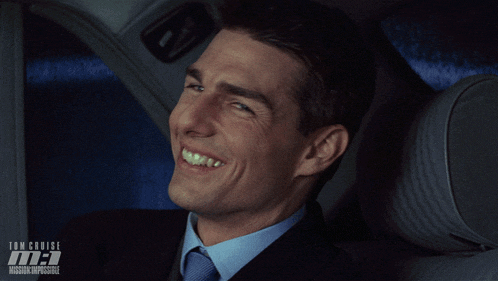 a man in a suit and tie is smiling in front of a poster for tom cruise 's movie mission impossible