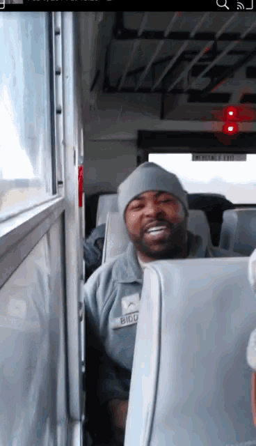 a man wearing a beanie and a name tag that says bigu sits on a bus