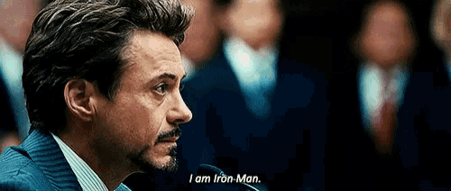 a man in a suit and tie is talking into a microphone and saying i am iron man .