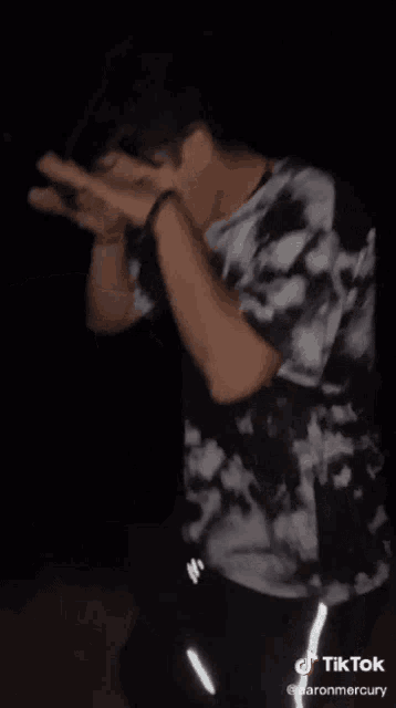 a man in a black and white tie dye shirt is dancing in the dark