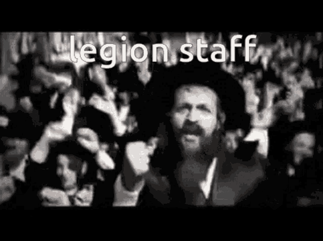 a man with a beard is standing in front of a crowd with legion staff written on the bottom