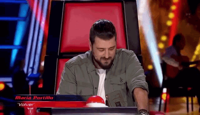 a man with a beard is sitting in a chair with a red button that says maria portillo