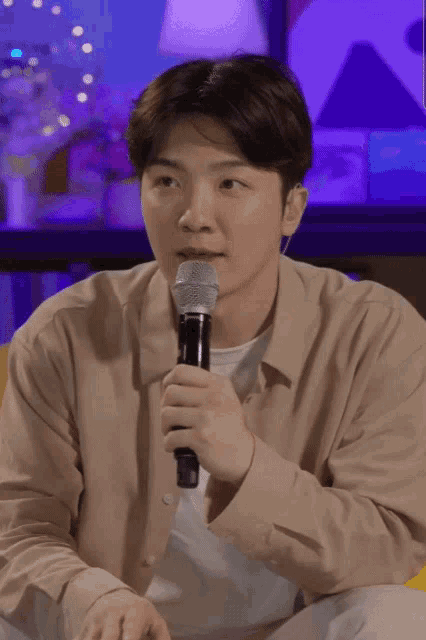 a man in a tan shirt holds a microphone in his right hand