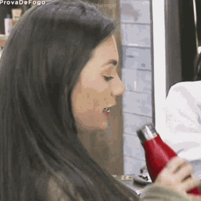 a woman with long black hair is holding a red water bottle in her hand .