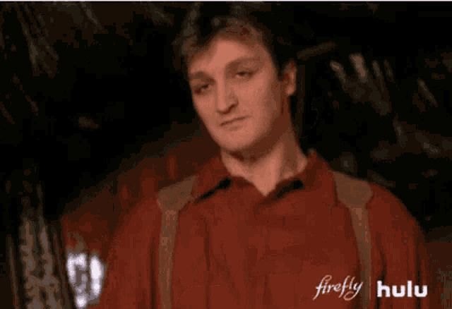 a man in a red jacket is sitting with his arms crossed and looking at the camera .