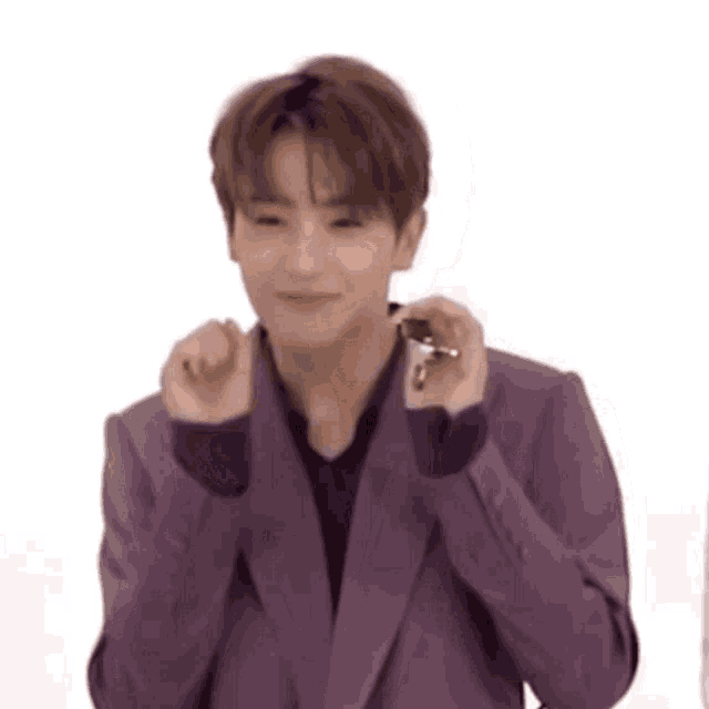 a young man in a purple jacket is making a heart shape with his hands .