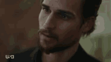 a close up of a man 's face with a beard wearing a black jacket .
