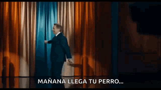 a man in a suit and tie is standing in front of a curtain and says mañana llega tu perro ..
