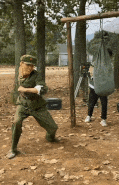a man in a military uniform is standing in a field with a bag hanging from a pole