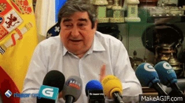 a man is sitting in front of a bunch of microphones and flags .