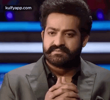 a man with a beard and mustache is wearing a suit and making a sad face .