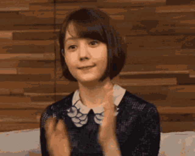 a woman with short hair is sitting on a couch with her hands folded in front of a wooden wall .