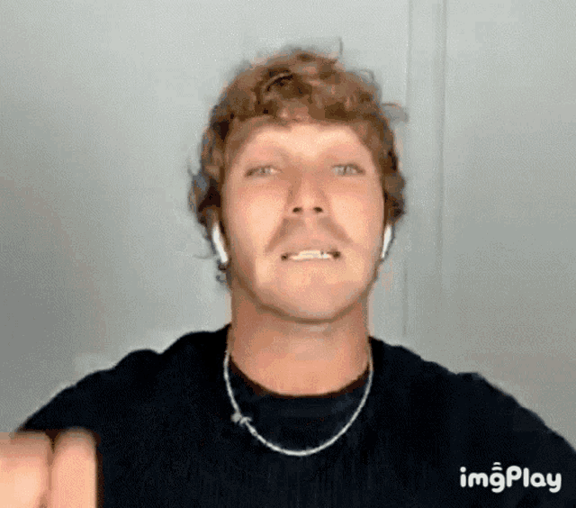 a man with curly hair is wearing headphones and a necklace while making a funny face .