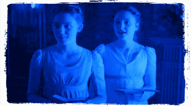 two women in white dresses are standing next to each other in a dark room