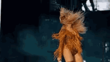 a woman in a gold costume is dancing on a stage in a dark room .