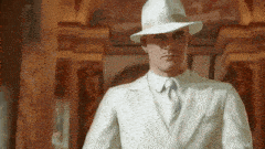 a man in a white suit and hat is standing in front of a wall .