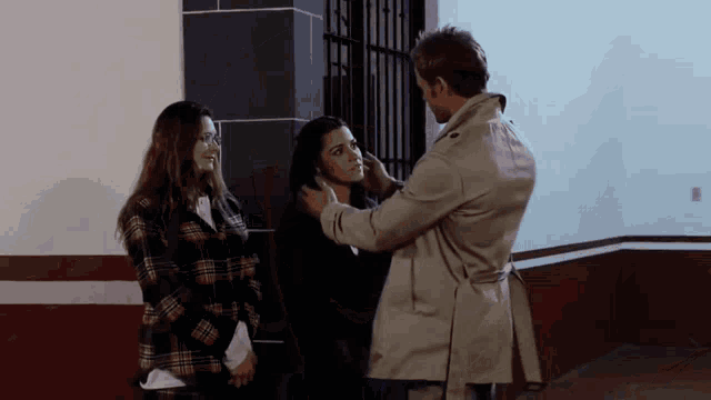 a man in a trench coat holds a woman 's face