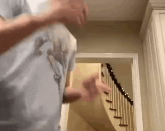 a man in a blue shirt is dancing in a room next to stairs .
