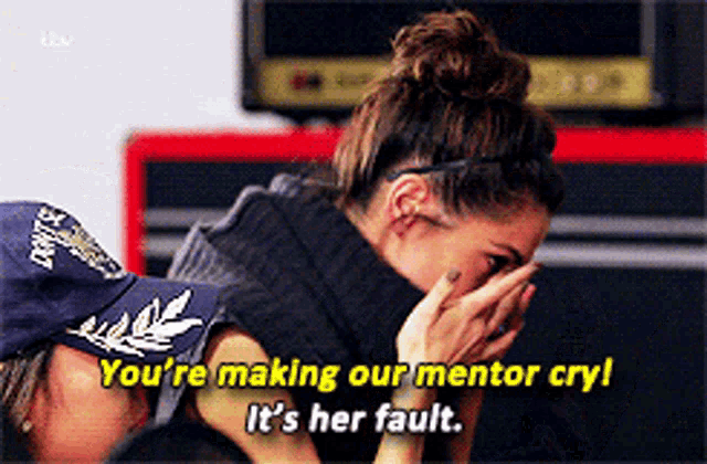 a woman covering her face while another woman says " you 're making our mentor cry "
