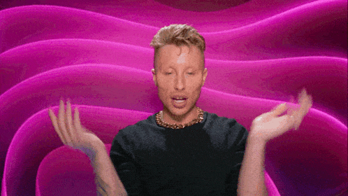 a man in a black shirt is standing in front of a pink background with his hands outstretched .