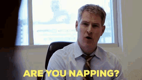 a man in a suit and tie is sitting at a desk and says are you napping ?