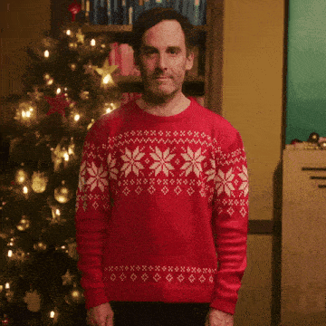 a man wearing a red sweater with white snowflakes on it stands in front of a christmas tree