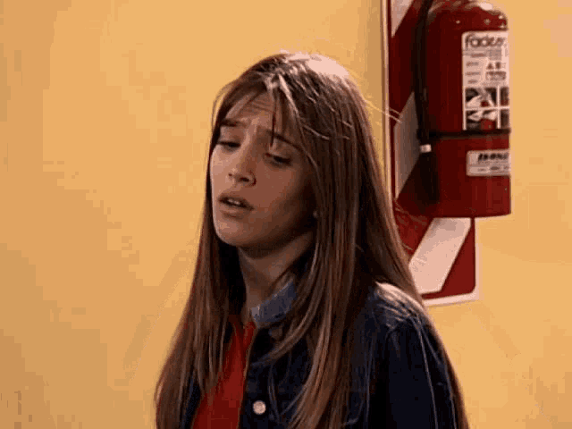 a woman is standing in front of a fire extinguisher on a yellow wall .