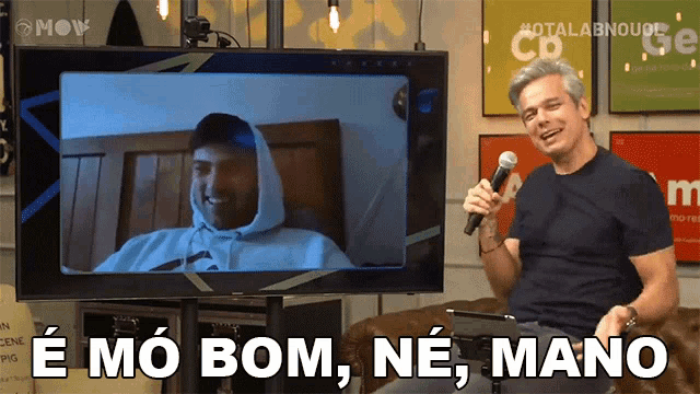 a man is holding a microphone in front of a tv screen that says " e mo bom ne mano "