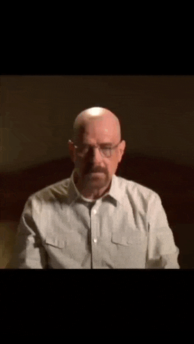 a bald man with glasses and a mustache is sitting in a dark room