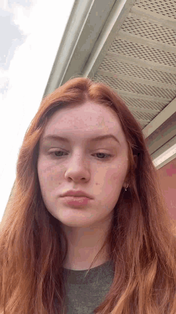a woman with red hair and freckles looks at the camera with a serious look on her face