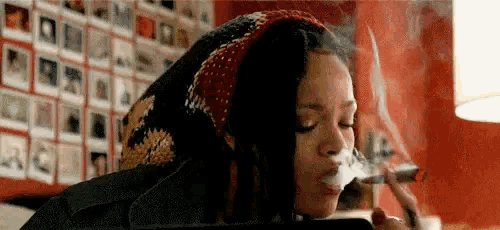 a woman is smoking a cigarette in a room with a lot of pictures on the wall .