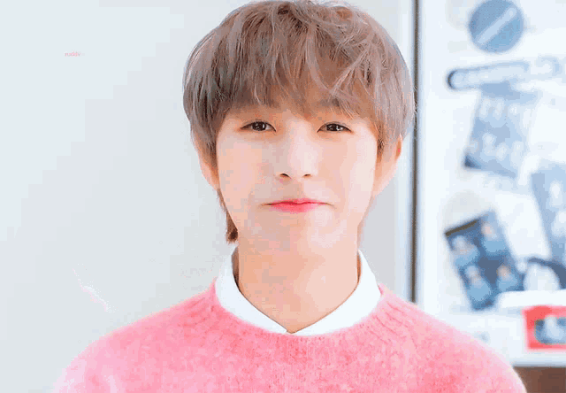 a young man wearing a pink sweater and a white shirt is giving a thumbs up
