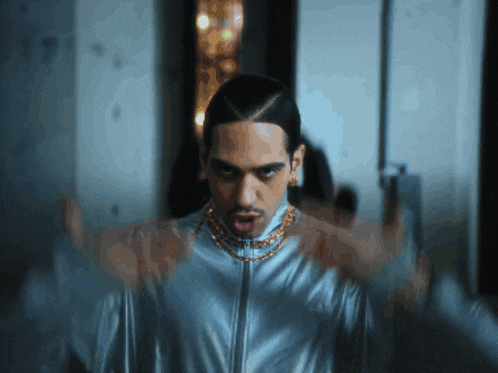 a man with a gold chain around his neck is standing in a dark room