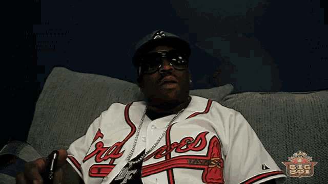 a man wearing a braves jersey sits on a couch in front of a big boy logo