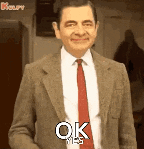 mr bean is wearing a suit and tie and is smiling and saying ok yes .