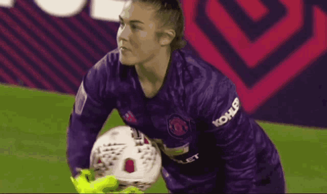 a woman in a purple jersey is holding a soccer ball on a field .