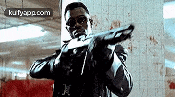 a man is holding a gun in a bloody room in a movie .