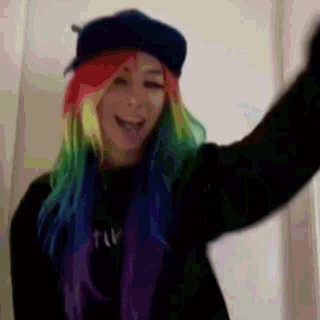 a woman with rainbow hair is wearing a black shirt and a black hat
