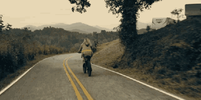 a person riding a bike down a road with mountains in the background and a white rv parked on the side of the road