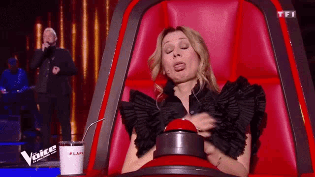 a woman is sitting in a red chair and pressing a button on a stage .