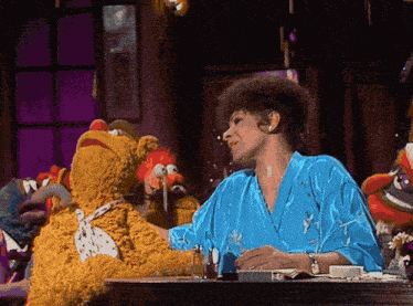 a woman in a blue robe is sitting at a table with stuffed animals
