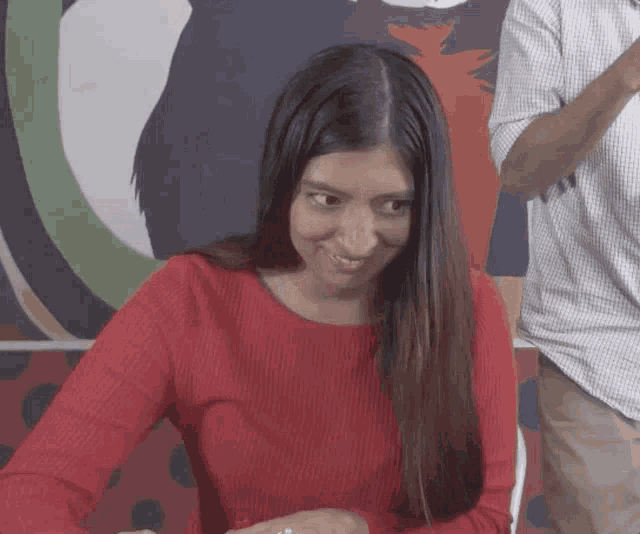 a woman in a red sweater is smiling with a man in a plaid shirt behind her