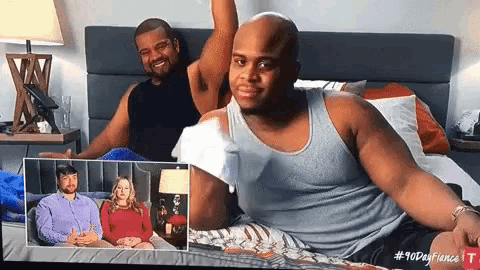 a man in a tank top is sitting on a bed next to a woman in a red shirt