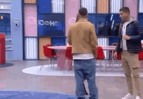 two men are standing in a room with tables and chairs .