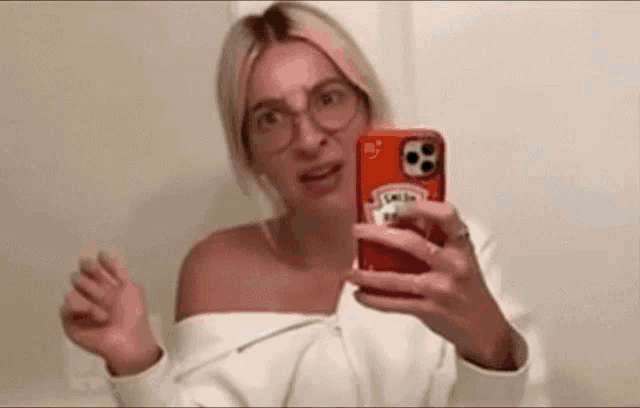 a woman wearing glasses is taking a selfie in front of a mirror .